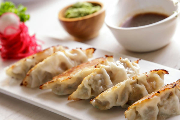 A platter of crispy pan-fried dumplings served with dipping sauce and pickled ginger.jpg