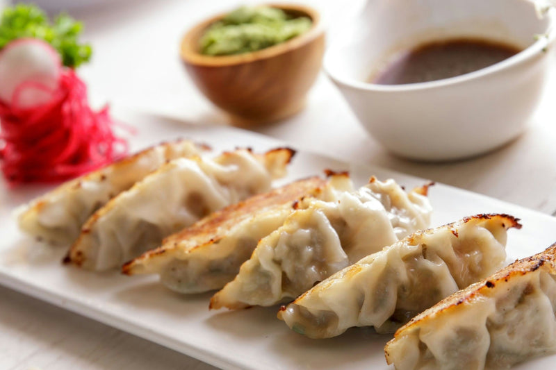 A platter of crispy pan-fried dumplings served with dipping sauce and pickled ginger.jpg