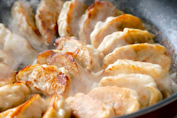 Dumplings sizzling in a pan, lightly browned and cooking in steam.jpg