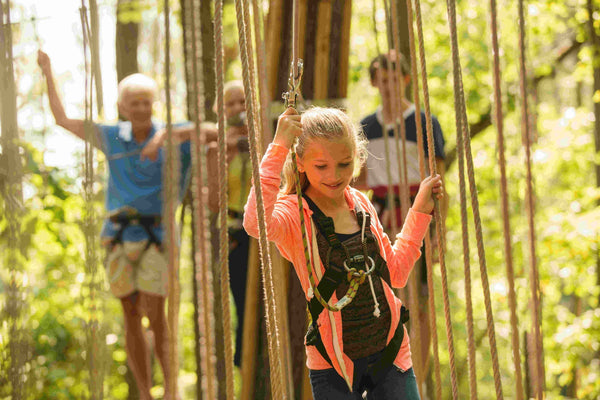 woman in a teal shirt going across a rope bridge