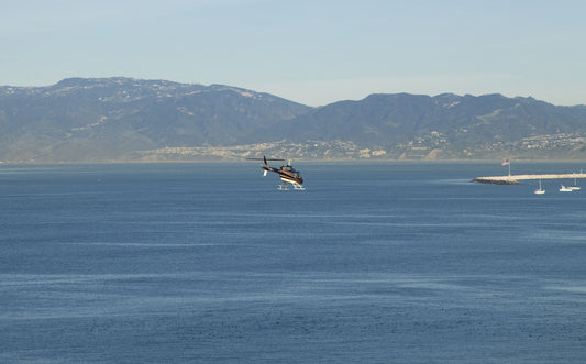 helicopter flying over water with mountain backdrop