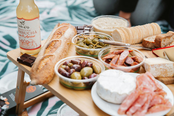 matcha tea, green olives, cheese, meat and bread on board on picnic blanket