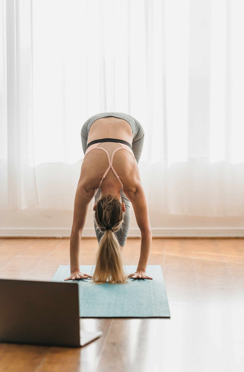 woman-doing-virtual-yoga-on-a-teal-mat-in-front-of-white-curtains