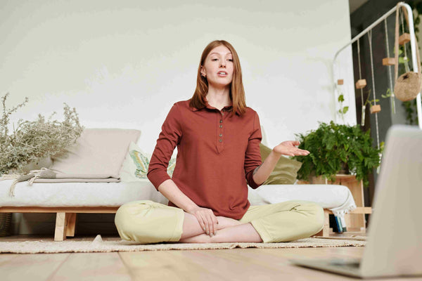 woman-in-orange-and-yellow-doing-virtual-yoga-in-her-living-room
