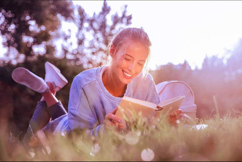 woman reading in a field in a blue shirt