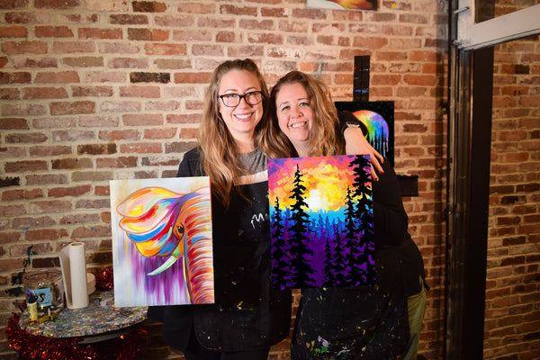 women with paintings by brick wall