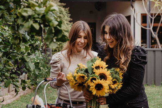 girls in beige and black shirts holding flowers